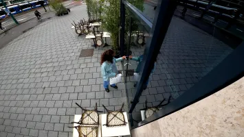 Mitarbeiterin schließt die Glastür eines Cafés, während vor dem Eingang Tische und Stühle hochgestellt sind – eine typische Schließsituation für eine Alarmanlage fürs Geschäft.