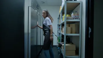 Mitarbeiterin in einem Lagerraum vor gewerblichen Kühlschränken, von denen eine Tür offensteht, als Beispiel für Sicherheitslösungen für Unternehmen in sensiblen Betriebsbereichen.