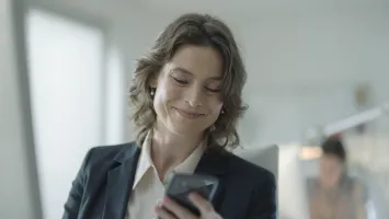 Securitas Connect im Büro per Smartphone Frau im Büro schaut auf ihr Smartphone und nutzt Securitas Connect zur mobilen Steuerung von Sicherheitsfunktionen.