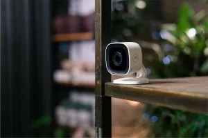 Eine weiße Überwachungskamera ist auf einem Regal in einem Geschäft oder Café positioniert und überwacht diskret die Umgebung im Innenraum.