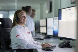 Eine Mitarbeiterin in Securitas-Uniform mit Headset überwacht mehrere Monitore in einer Notruf- und Serviceleitstelle, unterstützt durch ein Team im Hintergrund.