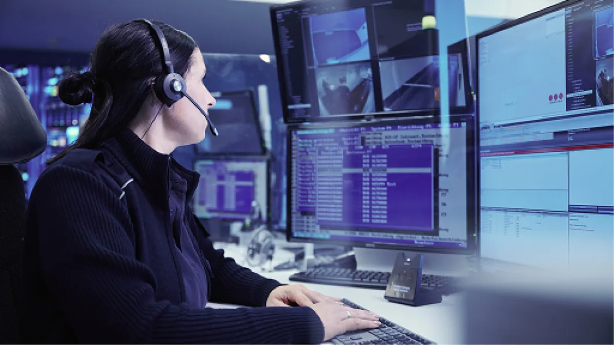 Mitarbeiterin der Securitas-Leitstelle mit Headset vor mehreren Monitoren
