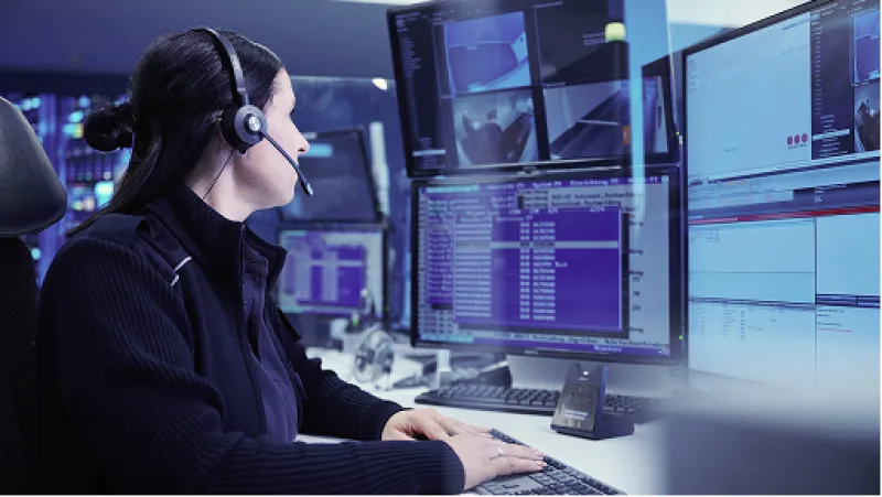 Mitarbeiterin der Securitas-Leitstelle mit Headset vor mehreren Monitoren